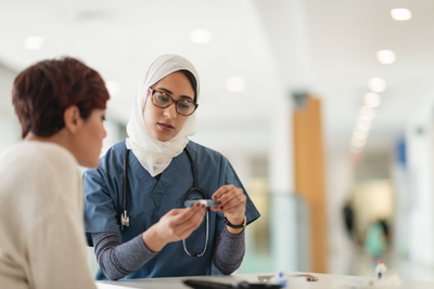 A female medical professional wearing a hijab talks with a client while holding a tool to help track and manage diabetes.