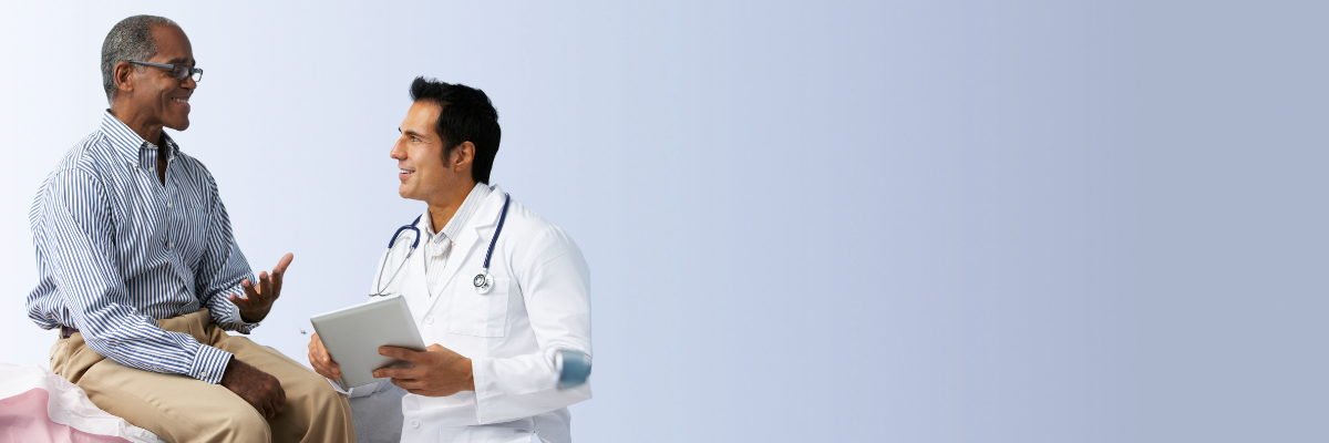 Healthcare professional in lab coat holding a notebook while listening to a seated patient.